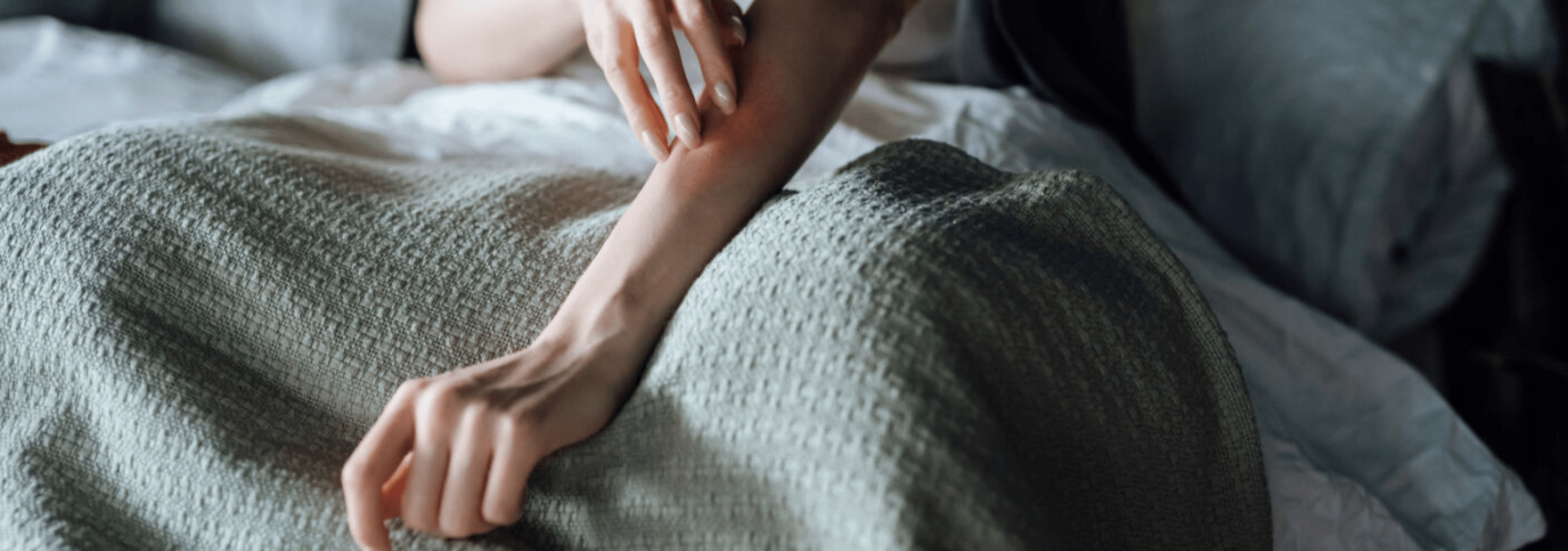 Woman scratching arm, possibly due to a bite or sting, with visible irritation.