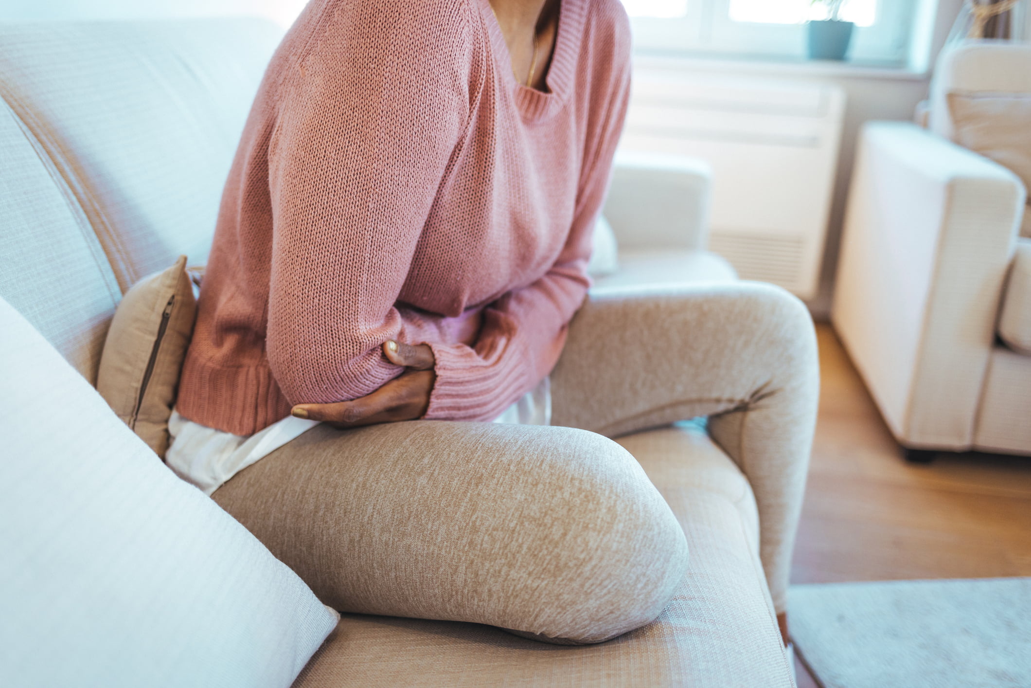 Woman sitting on a couch, holding her stomach with a pained expression, possibly due to a UTI.