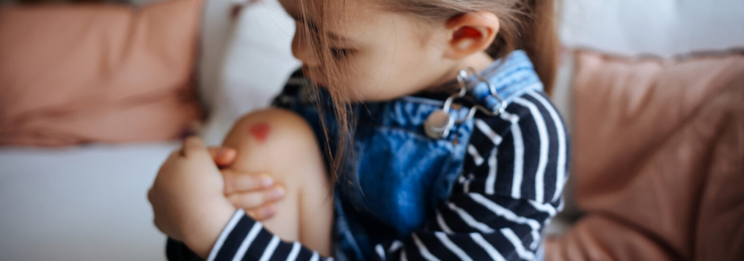 Child sitting on the ground, holding their scraped knee and showing a pained expression.