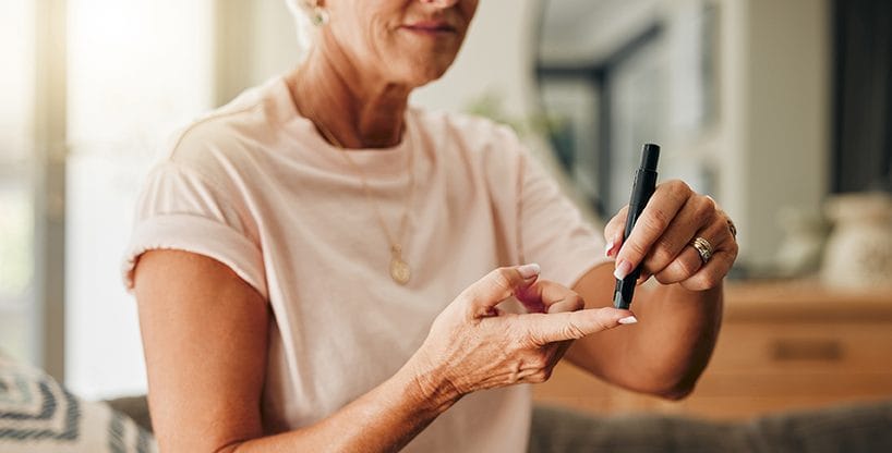 Diabetes, health and elderly woman doing a blood sugar test on her finger with a glucometer. Sickness, healthcare and diabetic senior lady checking her glucose level sitting on a sofa at home